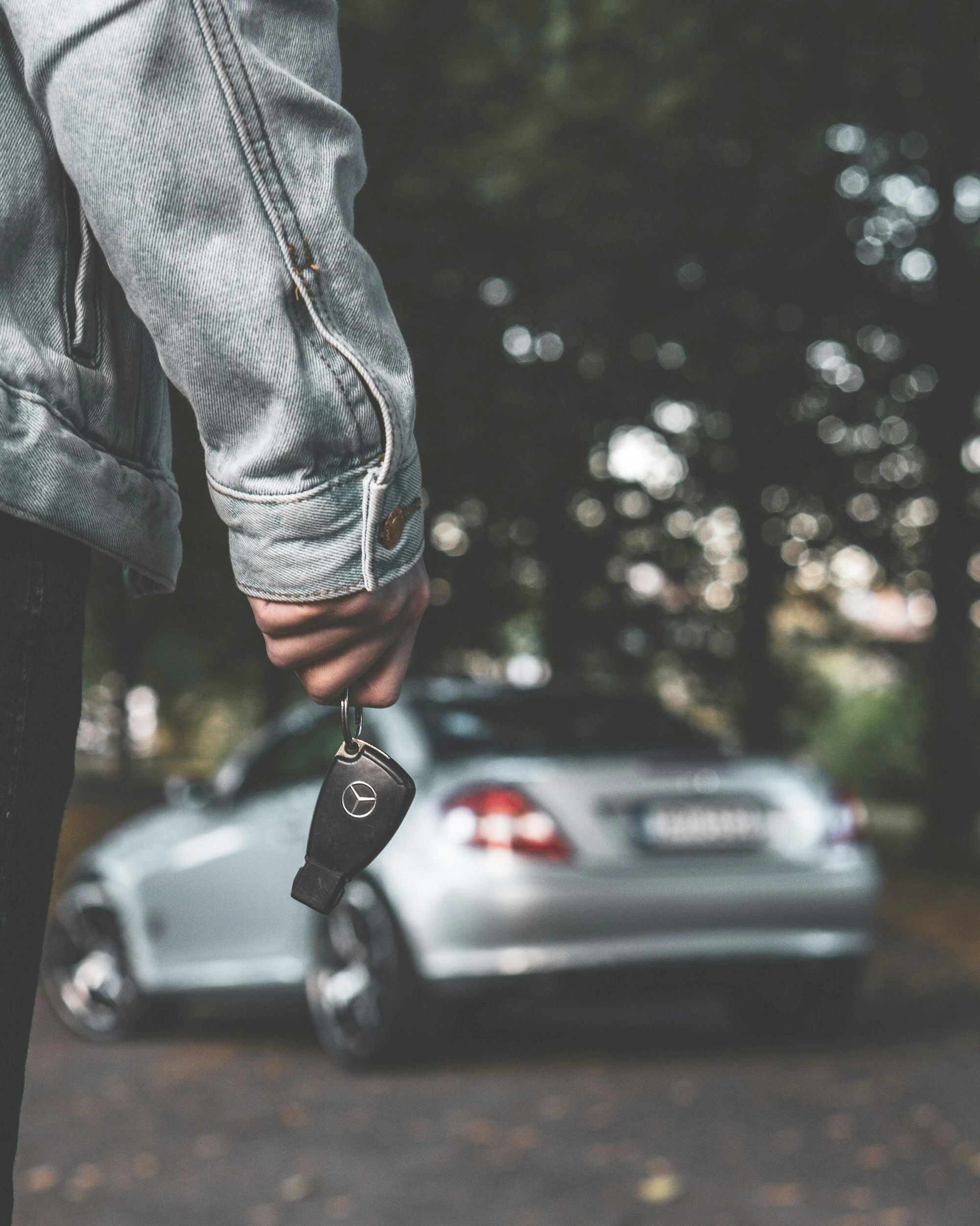 Mão segurando a chave ao lado de um carro prata