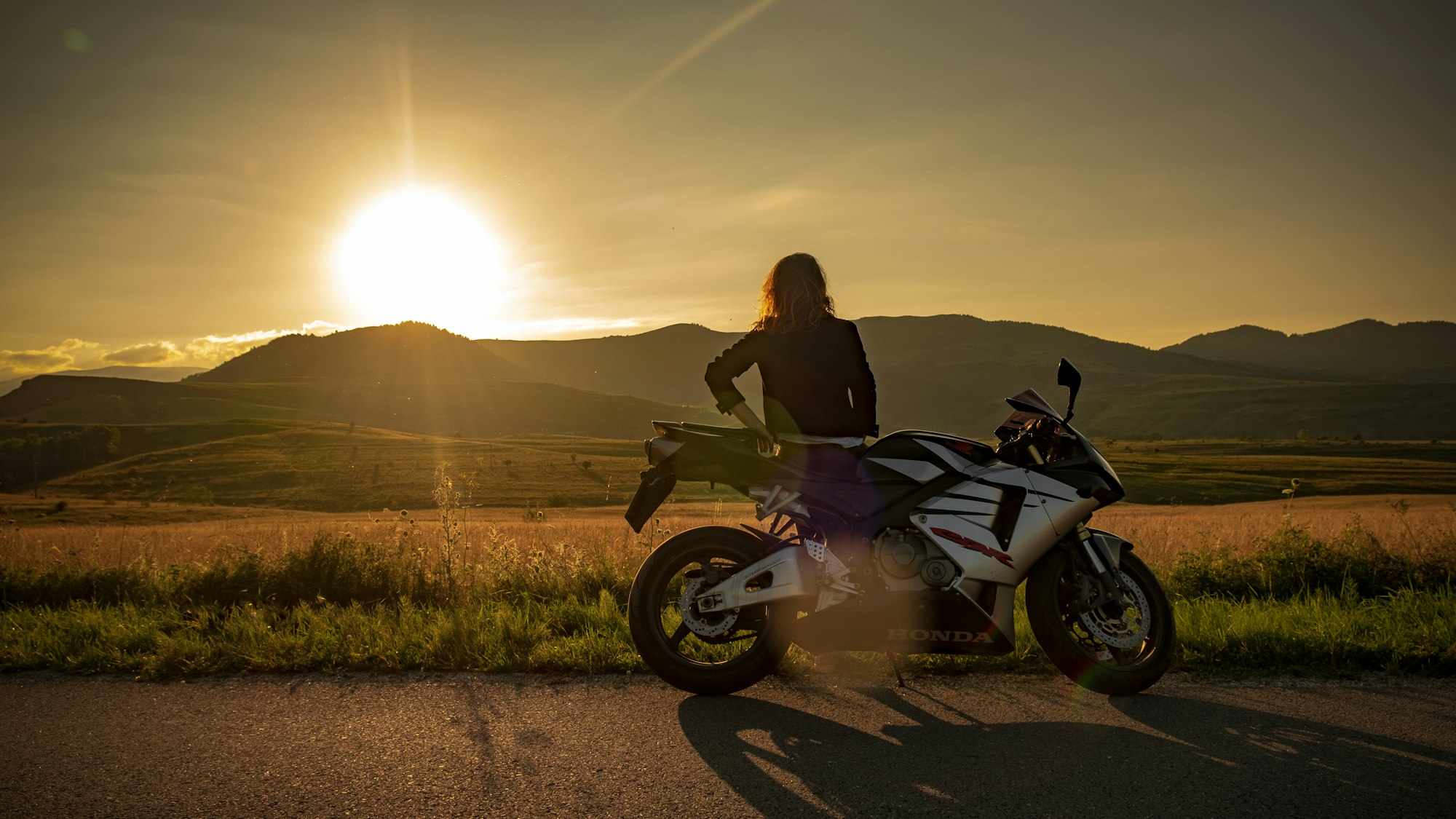 Motociclista parada ao lado da moto ao pôr do sol