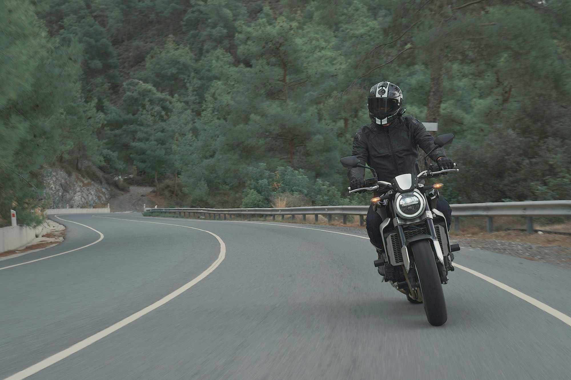 Motociclista fazendo uma curva em uma estrada cercada de árvores
